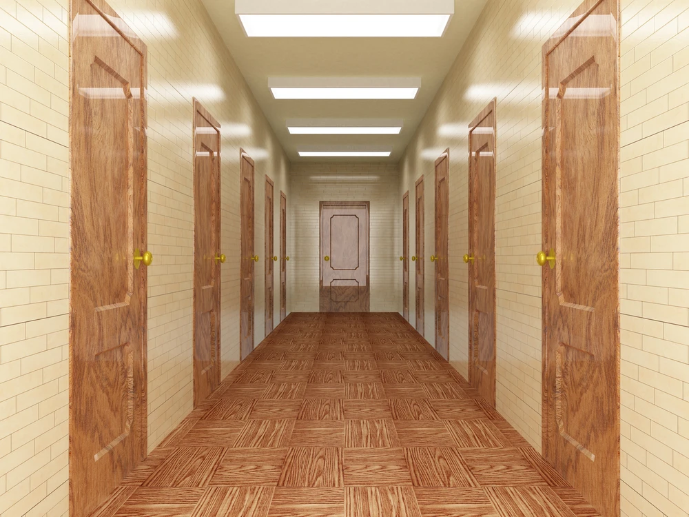 Couloir institutionnel avec portes en bois alignées de chaque côté, sol en parquet à motifs géométriques, murs carrelés beige, éclairage fluorescent encastré au plafond