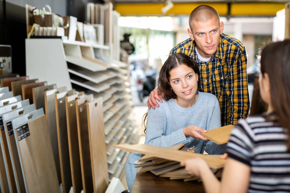 Magasin de revêtements de sol avec couple consultant échantillons de parquet et stratifié auprès d'une vendeuse