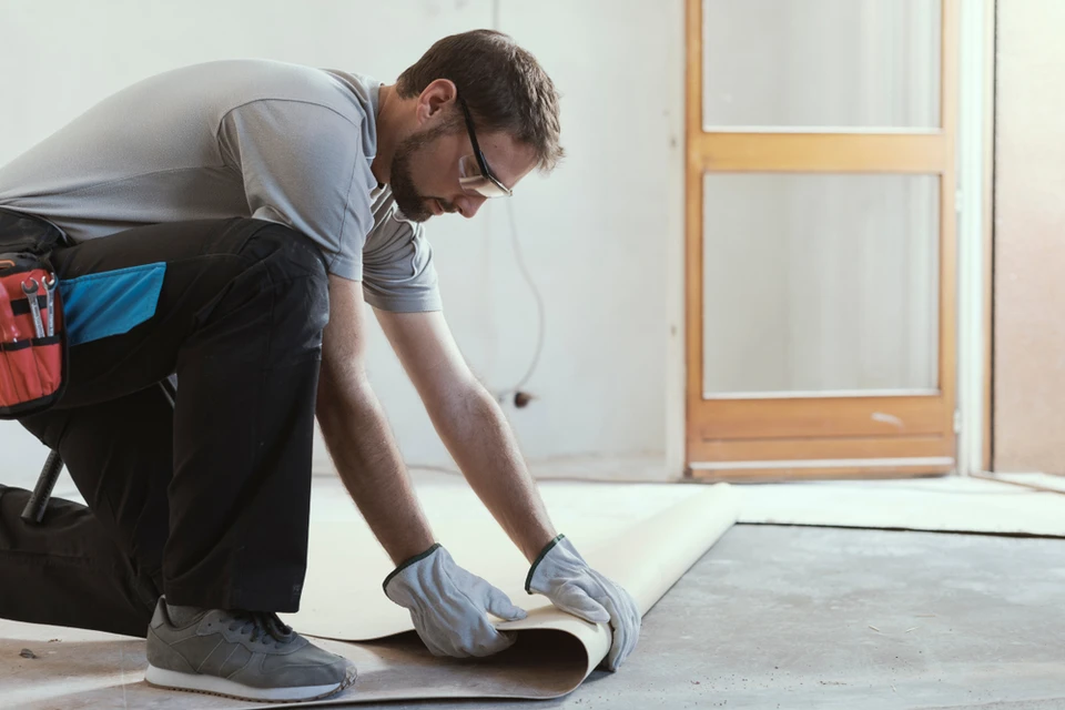 Homme en tenue de travail installant un revêtement de sol dans un intérieur résidentiel moderne